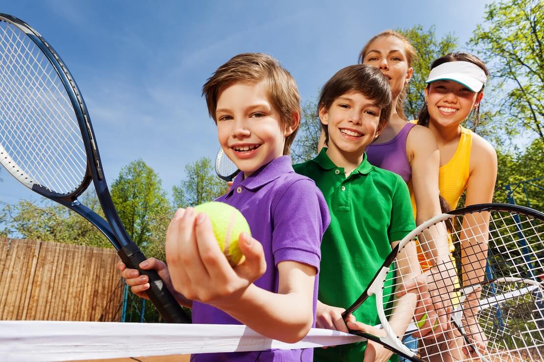 Vier Kinder stehen hintereinander mit einem Tennisball und Schläger